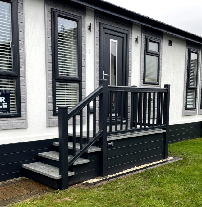 Dark grey and white holiday lodge with steps and grass.