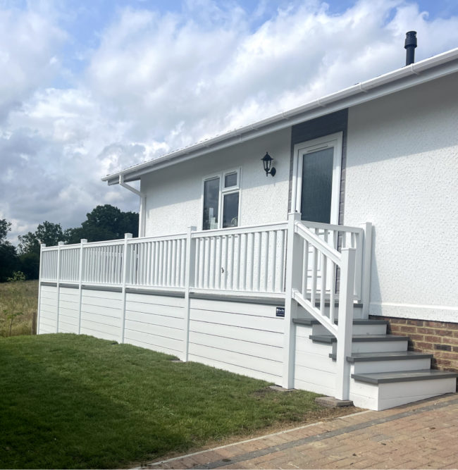 White holiday home with steps and white banner, deckboard and grass