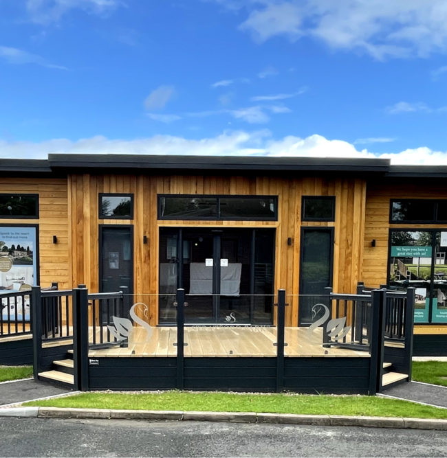Wooden and black commercial property with glass and black handrails, grass in the front and pavement out the front